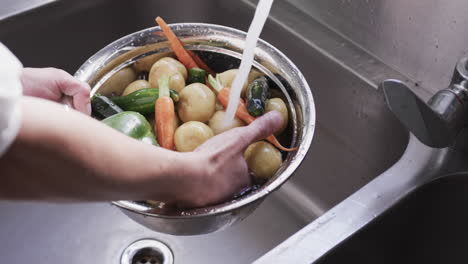 African-american-male-chef-washing-vegetables-in-sink-in-kitchen,-slow-motion