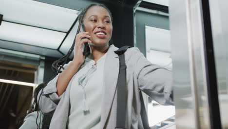 Feliz-Mujer-De-Negocios-Afroamericana-Casual-Hablando-Por-Teléfono-Inteligente-En-Ascensor,-Cámara-Lenta