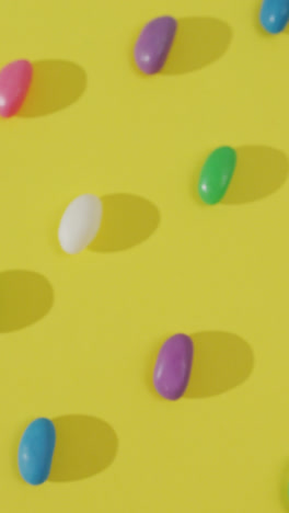 Video-of-overhead-view-of-rows-of-multi-coloured-sweets-over-yellow-background