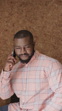 Vertical-video-portrait-of-happy-african-american-casual-businessman-talking-on-smartphone-in-office