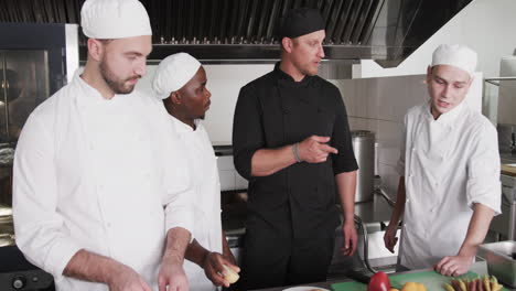 Diverse-male-chef-instructing-group-of-trainee-male-chefs-in-kitchen,-slow-motion