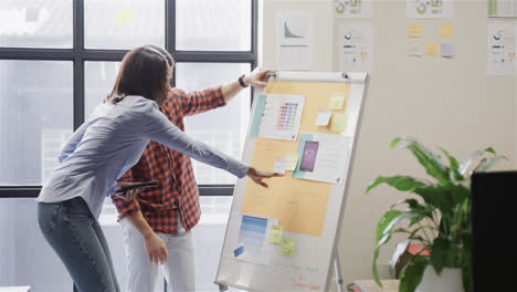 Diverse-male-and-female-colleagues-standing-at-board,-talking-and-using-tablet