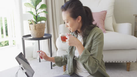 Mujer-Asiática-Feliz-Bebiendo-Té-Y-Usando-Una-Tableta-En-El-Dormitorio,-En-Cámara-Lenta