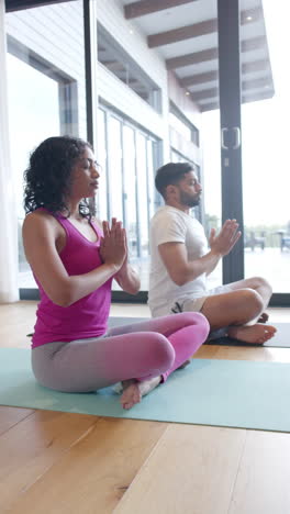 Vertical-video-of-biracial-couple-doing-yoga-and-meditating-at-home,-in-slow-motion