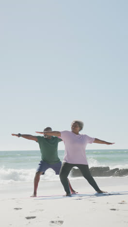 Video-Vertical-De-Una-Pareja-Afroamericana-Haciendo-Yoga-En-La-Playa,-En-Cámara-Lenta