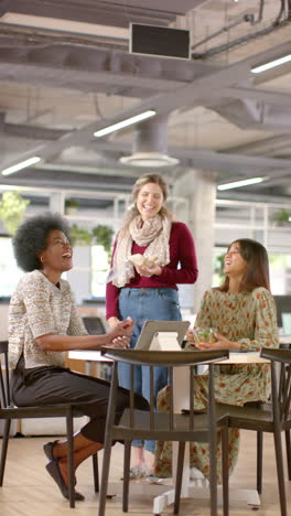 Vertical-video-of-happy-diverse-female-colleagues-discussing-using-tablet-in-office,-slow-motion