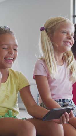 Video-of-diverse-girls-sitting-at-school-common-room-with-smartphone,-talking-and-laughing