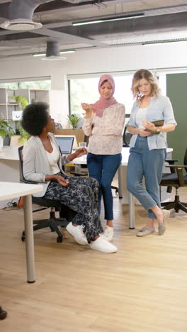 Vertical-video-of-diverse-female-creative-colleagues-discussing-using-tablet-in-office,-slow-motion