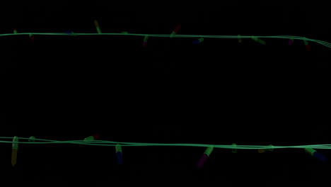 Coloured-christmas-string-lights-flashing-on-black-background,-copy-space