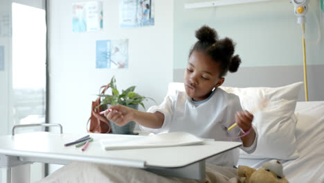 Niña-Afroamericana-Dibujando-En-Un-Cuaderno-En-La-Cama-De-Un-Hospital,-En-Cámara-Lenta