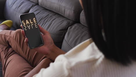 Biracial-woman-on-couch-using-smartphone-online-shopping-during-sale,-slow-motion