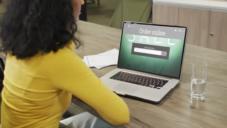 Biracial-woman-at-table-using-laptop,-online-shopping-during-sale,-slow-motion