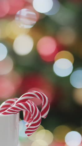 Vertical-video-of-mug-of-christmas-candy-canes-with-christmas-tree-background