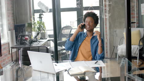 African-american-casual-businessman-sitting-at-desk-talking-on-smartphone-at-home,-slow-motion