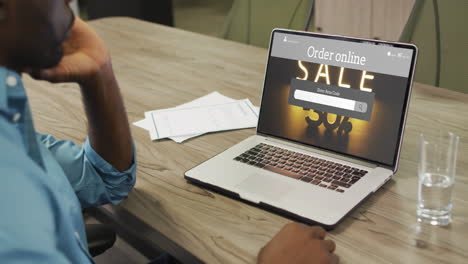 African-american-man-at-table-using-laptop,-online-shopping-during-sale,-slow-motion