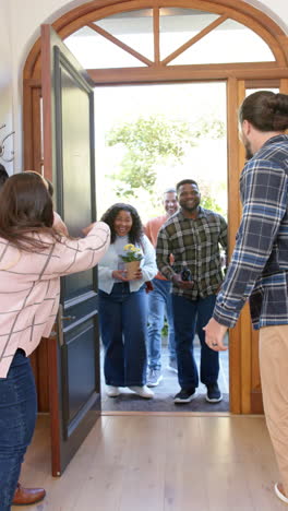 Vertical-video-of-happy-diverse-couple-welcoming-friends-in-sunny-house