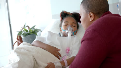 Mujer-Afroamericana-Con-Mascarilla-Acariciando-A-Su-Hija-Con-Máscara-De-Oxígeno-En-El-Hospital,-Cámara-Lenta