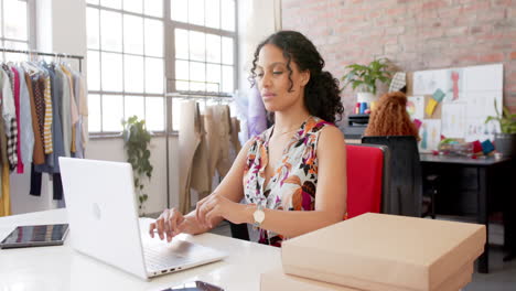 Portrait-of-happy-biracial-female-fashion-designer-using-laptop-at-desk-in-studio,-slow-motion