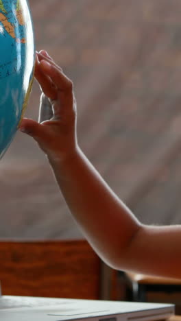 Vertical-video-of-a-child's-hand-touching-a-globe-in-a-classroom-setting