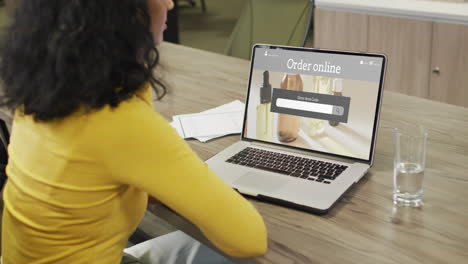 Biracial-woman-at-table-using-laptop,-online-shopping-for-beauty-products,-slow-motion