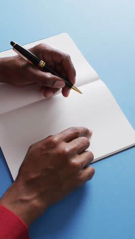 Vertical-video-of-hand-writing-with-pen-on-book-with-copy-space-on-blue-background-in-slow-motion