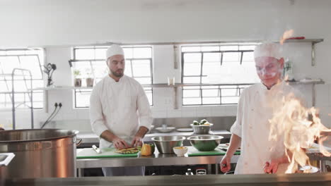 Grupo-De-Chefs-Masculinos-Diversos-Enfocados-Preparando-Comidas-Con-Fuego-Explosivo-En-La-Cocina,-Cámara-Lenta