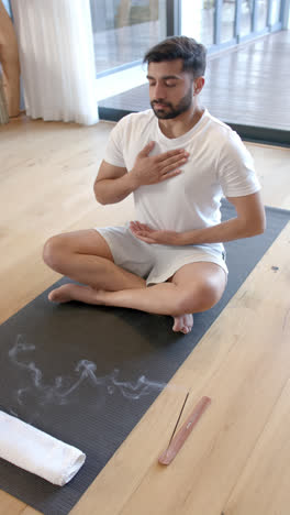 Vertical-video-of-biracial-man-doing-yoga-and-meditating-at-home,-slow-motion
