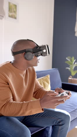 Video-Vertical-De-Un-Hombre-Afroamericano-Usando-Auriculares-Vr-Y-Jugando-Videojuegos-En-Casa,-Cámara-Lenta