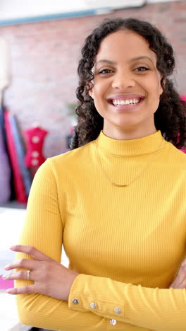 Portrait-of-happy-diverse-female-fashion-designer-with-arms-crossed-in-studio,-slow-motion,-vertical