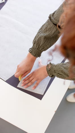 Vertical-video-of-biracial-female-fashion-designer-using-pattern-marking-cloth-with-chalk