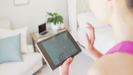 Asian-woman-using-tablet-with-smart-home-interface-in-bedroom,-in-slow-motion