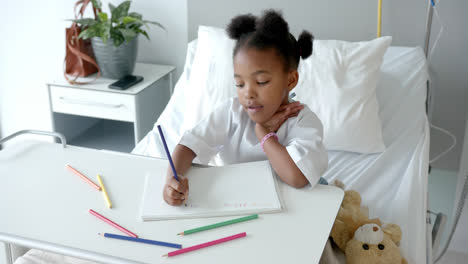 Niña-Afroamericana-Dibujando-En-Un-Cuaderno-En-La-Cama-De-Un-Hospital,-En-Cámara-Lenta