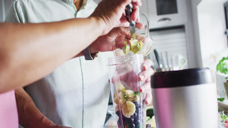 Senior-biracial-couple-preparing-healthy-drink-in-kitchen