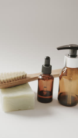 Vertical-video-of-close-up-of-glass-bottles,-soap-and-brush-and-copy-space-on-beige-background