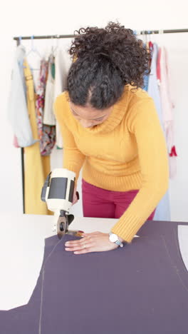 Diverse-female-fashion-designer-using-rotary-fabric-cutter-in-studio,-slow-motion,-vertical