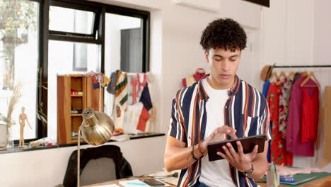 Diseñador-De-Moda-Masculina-Birracial-Usando-Una-Tableta-En-El-Estudio,-Cámara-Lenta