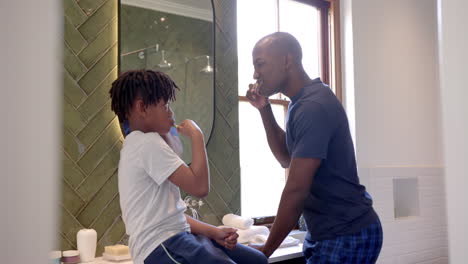 African-american-father-and-son-brushing-teeth-in-bathroom-at-home,-slow-motion