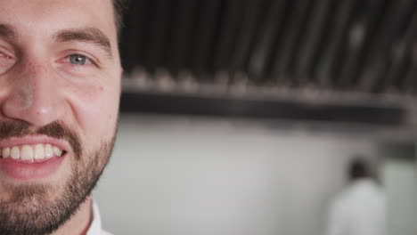 Half-portrait-of-happy-caucasian-male-chef-with-beard-smiling-in-kitchen,-copy-space,-slow-motion