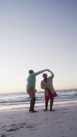 Vertical-video-of-senior-african-american-couple-dancing-at-beach,-in-slow-motion