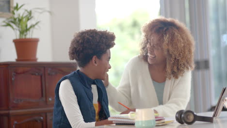 Happy-african-american-mother-helping-her-son-with-homework-using-tablet-in-kitchen,-slow-motion