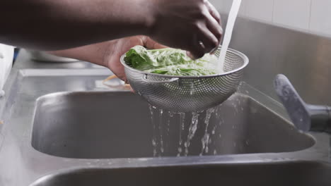 African-american-male-chef-washing-vegetables-in-sink-in-kitchen,-slow-motion