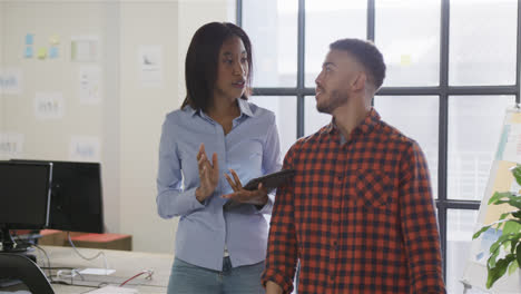 Diverse-male-and-female-colleagues-using-tablet-and-walking-through-office-talking