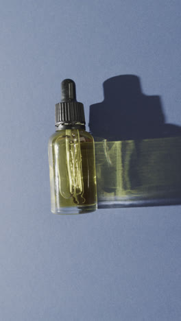 Vertical-video-of-close-up-of-glass-bottle-with-pumps-and-copy-space-on-blue-background