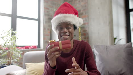 Feliz-Hombre-Afroamericano-Con-Sombrero-De-Santa-Sentado-En-Un-Sofá-Teniendo-Videollamada-En-Casa,-Cámara-Lenta