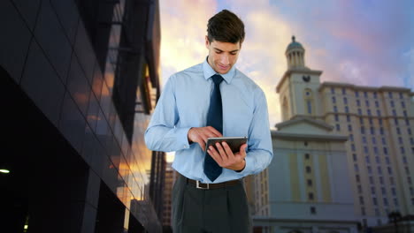 Vista-Compuesta-De-Un-Hombre-De-Negocios-Birracial-Usando-Una-Tableta-Digital-Contra-Edificios-Altos-Y-El-Cielo-Del-Atardecer