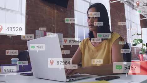 Animación-De-íconos-De-Redes-Sociales-Flotando-Contra-Una-Mujer-Birracial-Usando-Una-Computadora-Portátil-En-La-Oficina