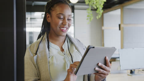 Happy-african-american-casual-businesswoman-using-tablet-standing-in-office,-slow-motion