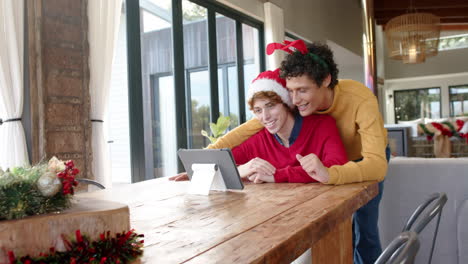 Pareja-Masculina-Gay-Diversa-Usando-Tableta-Para-Videollamadas-En-Casa-En-Navidad,-Cámara-Lenta