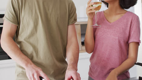 Video-of-happy-diverse-couple-preparing-meal-together-and-drinking-wine