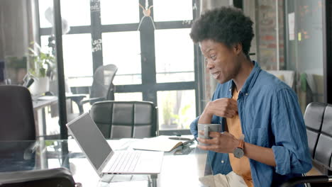 Happy-african-american-casual-businessman-at-desk-having-laptop-video-call-and-coffee,-slow-motion